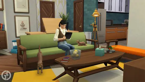 A Sim sat on a couch using a tablet surrounded by two cats