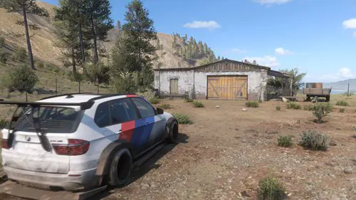 A car faces a barn in a desert setting.